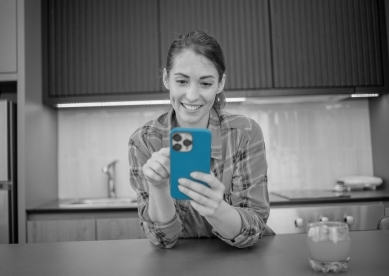 Woman sitting in her kitchen using her cell phone with a glass of orange juice next to her